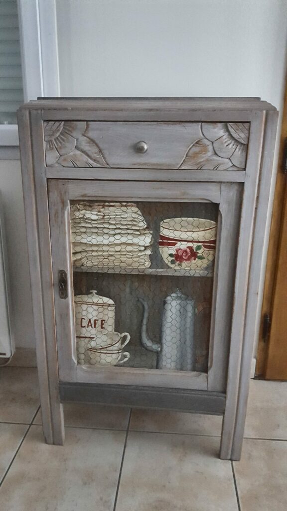 trompe-oeil-tasses-chiffons Trompe-l'œil sur meuble représentant des tasses, chiffons et cafetière derrière un grillage